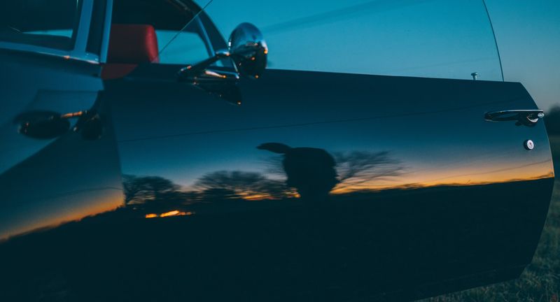 Sunset and silhouette mirrored in dark blue car door