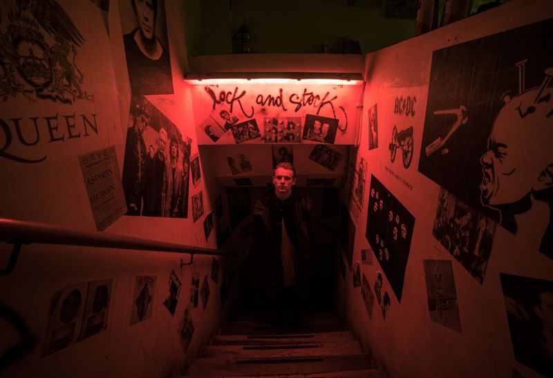 Red-lit rock-poster stairwell, man waiting below