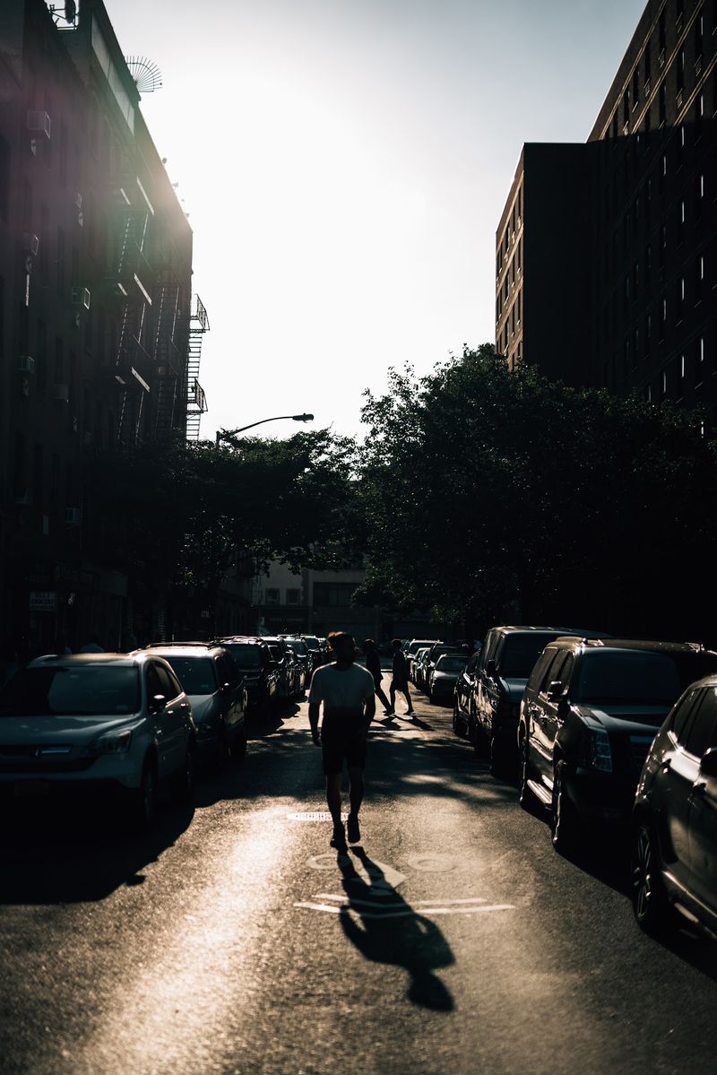 Lone walker and long shadow into backlit city street