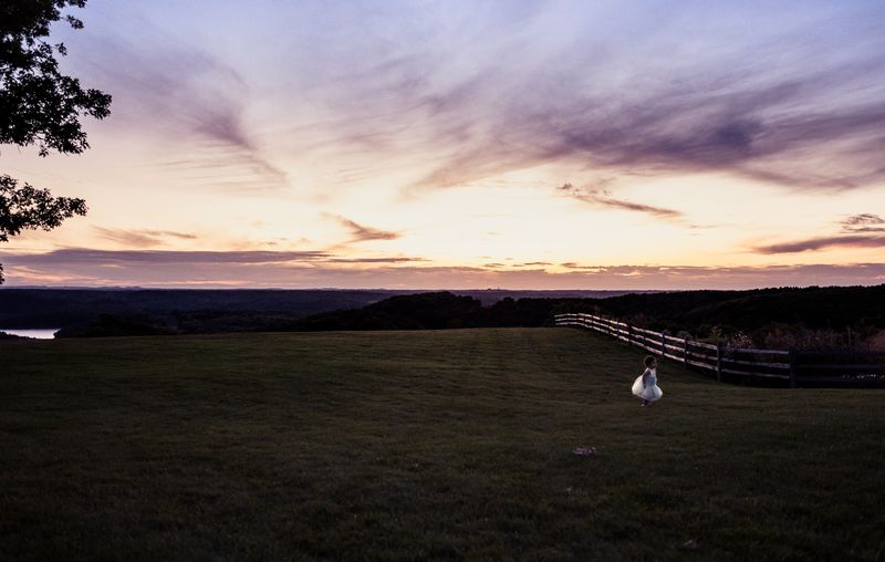 Streaked violet sunset over dark lawn, tiny figure in white
