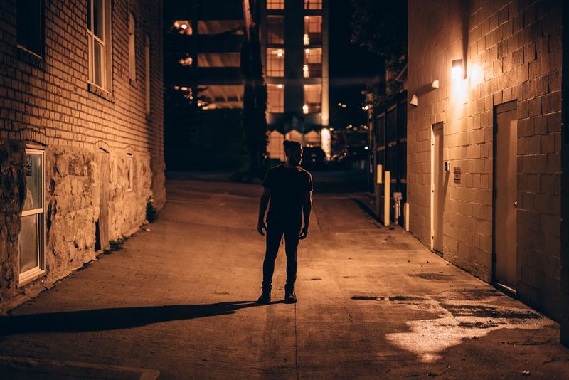 Lone man in warm-lit brick alley at night
