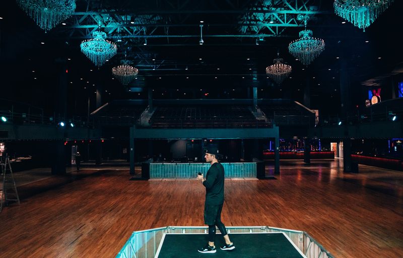 Lone figure crossing an empty floor under teal chandeliers