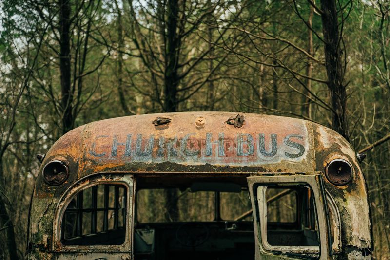 Rusted CHURCH BUS lettering on a wreck in the woods