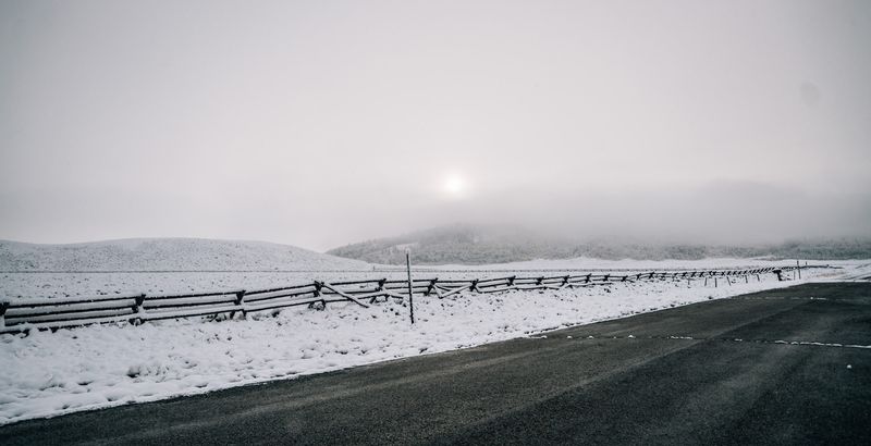 Pale sun over snowy fence line and empty road