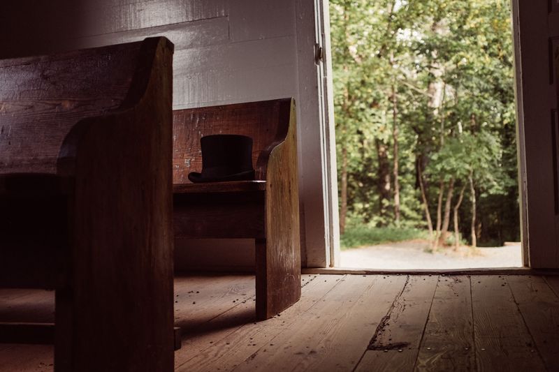 Top hat on a church pew, door open to green trees