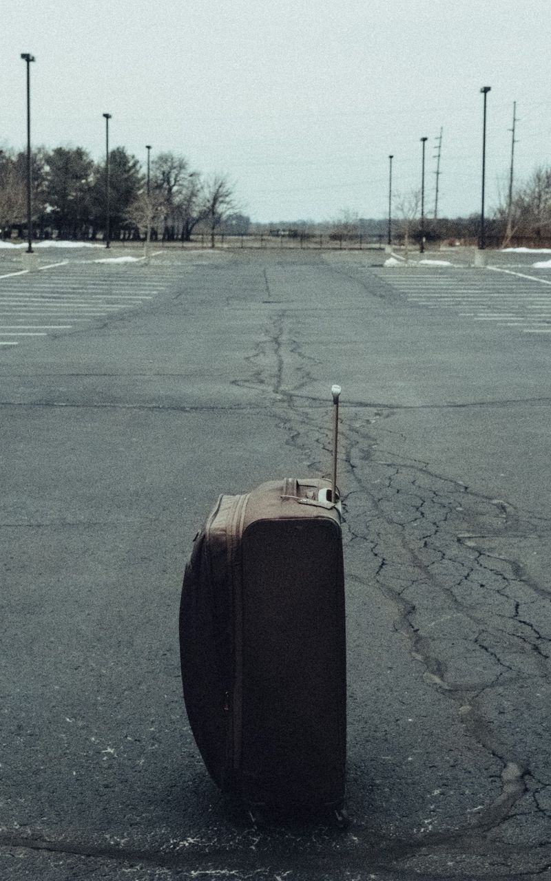 Lone suitcase upright in an empty cracked parking lot