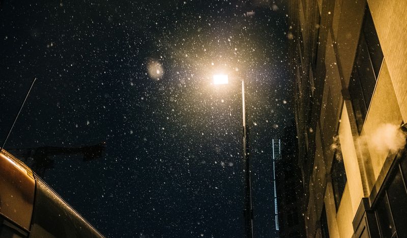 Snowflakes swirling around a streetlamp against black sky