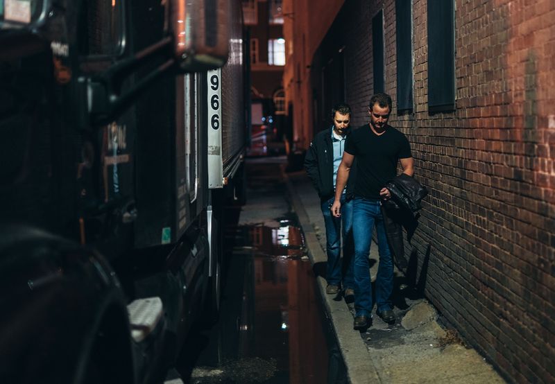 Easton walking wet brick alley beside tour bus at night