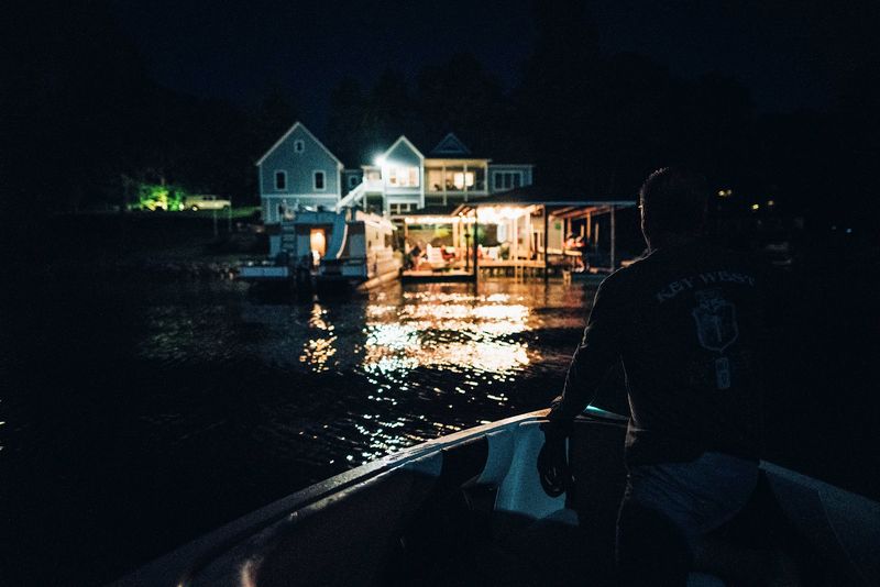 Silhouetted captain steering toward lit lakehouses