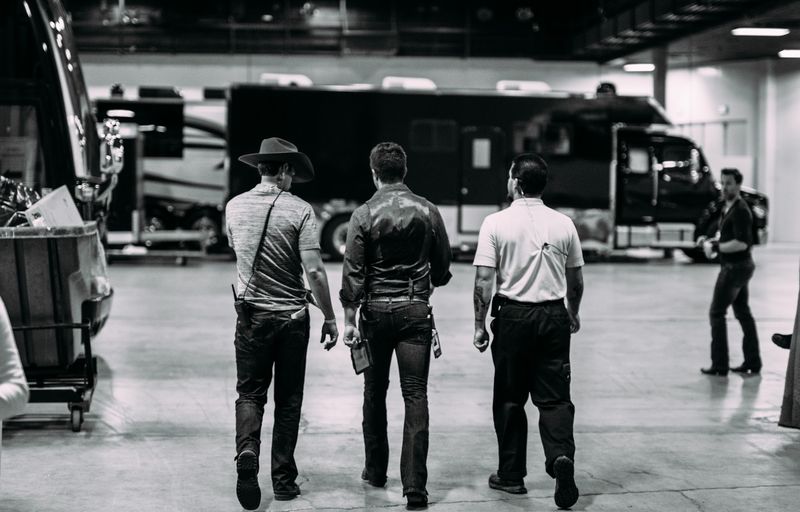 Monochrome trio walks toward tour buses, hat and vest