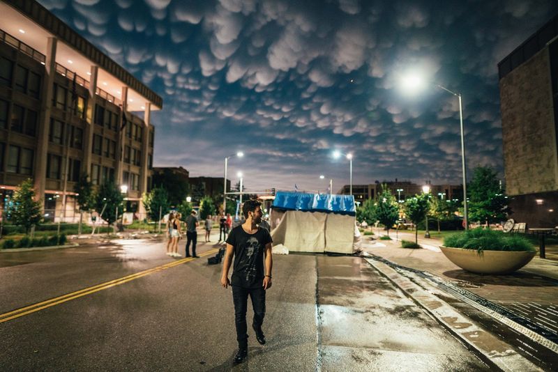Lone bandmate walking wet street under mammatus sky