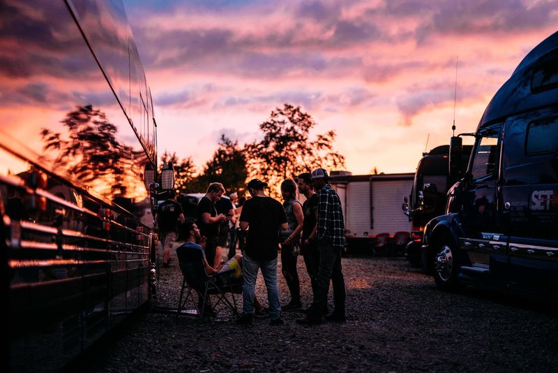 Backstage lot gathering between buses under fiery sky