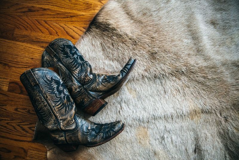 Tooled cowboy boots tossed on cowhide and hardwood