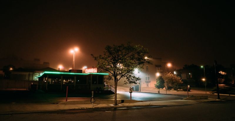 Night diner with green neon, sodium streetlights, empty corner