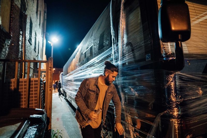 Bandmate grinning beside plastic-wrapped bus at night