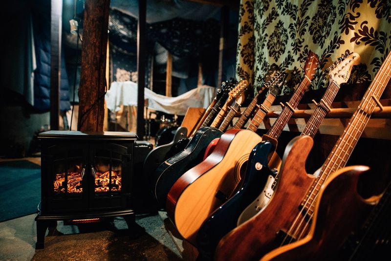 Guitars racked by glowing wood stove, damask wall