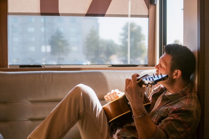 AJ playing harmonica and guitar in bus window light