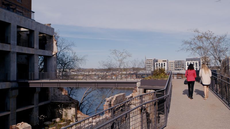 Two women walking riverside path past concrete mill
