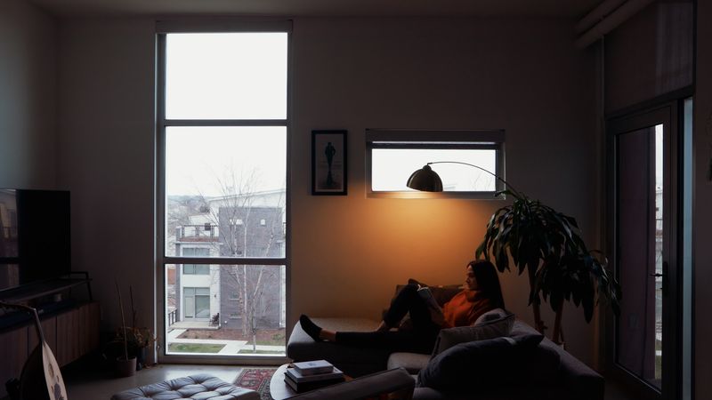 Woman reading on sofa beside tall window, lamplit