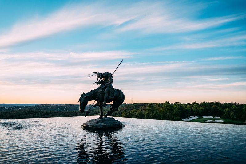 Sculpture reflected in infinity pool under streaked blue sky