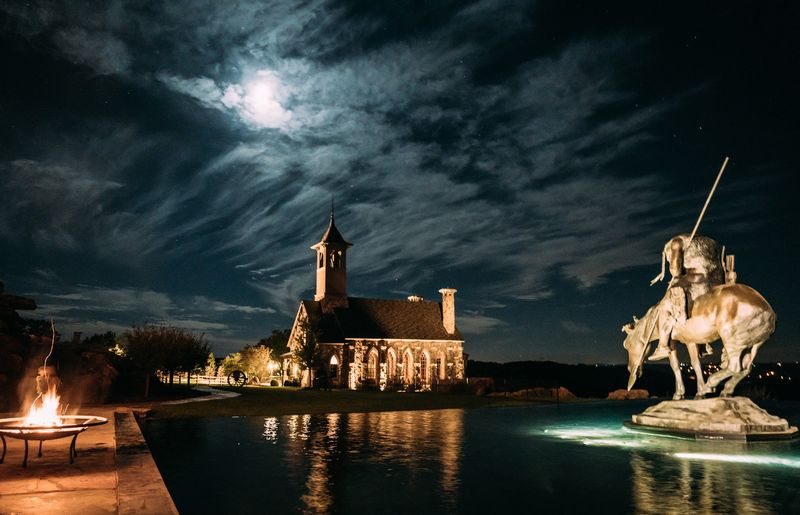 Fire pit, lit chapel and sculpture under moonlit clouds