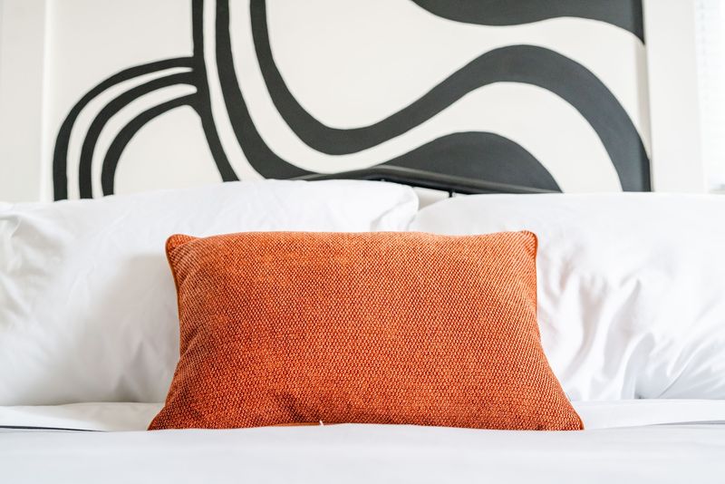 Orange pillow centered under black wave headboard art