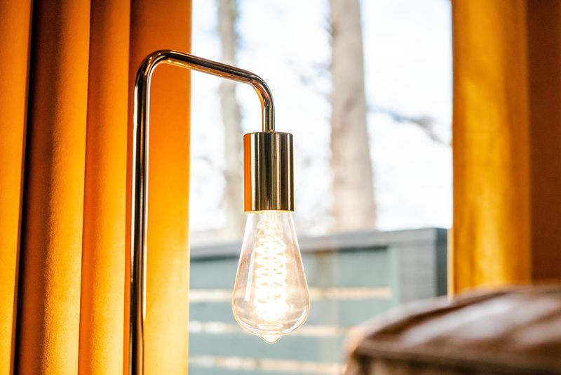Edison bulb glowing against window and gold drape
