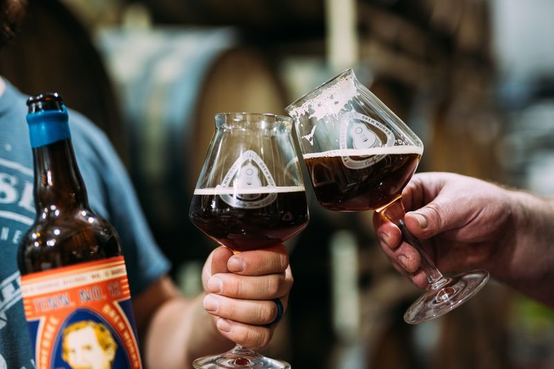 Close snifter clink, bottle foreground, barrels behind