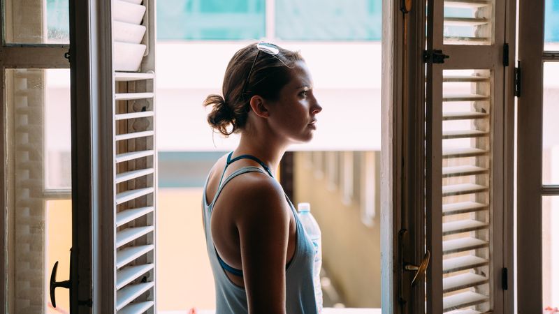 Woman in profile between wooden shutters, backlit window