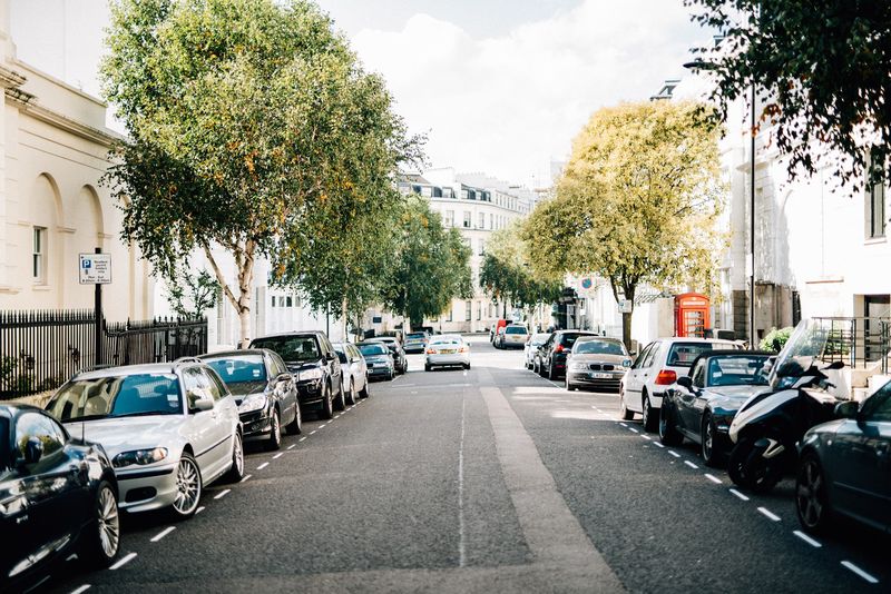 An empty terraced street of white houses and plane trees, a red phone box far down
