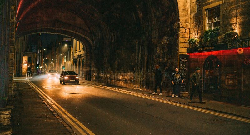 Arch tunnel at night, car light streaks, walkers