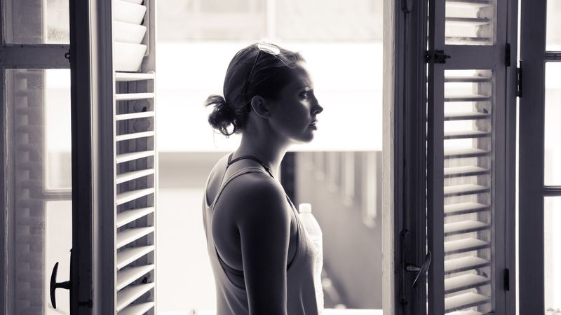 Profile between tall louvered shutters, window light, quiet monochrome