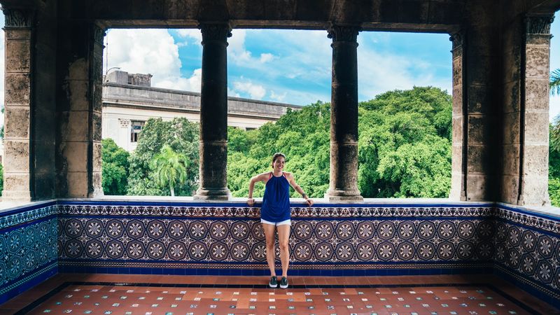 Small figure on a tiled balcony between dark columns, green trees