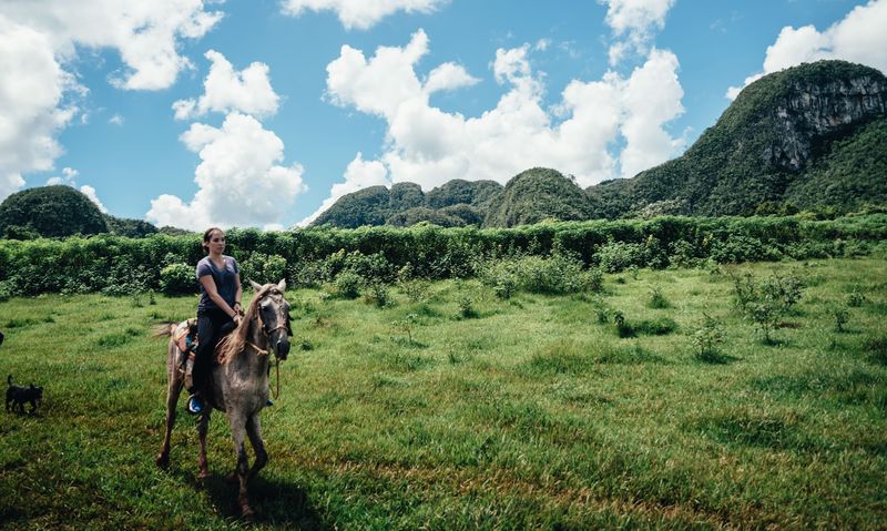 Woman on a horse in a green meadow below limestone hills
