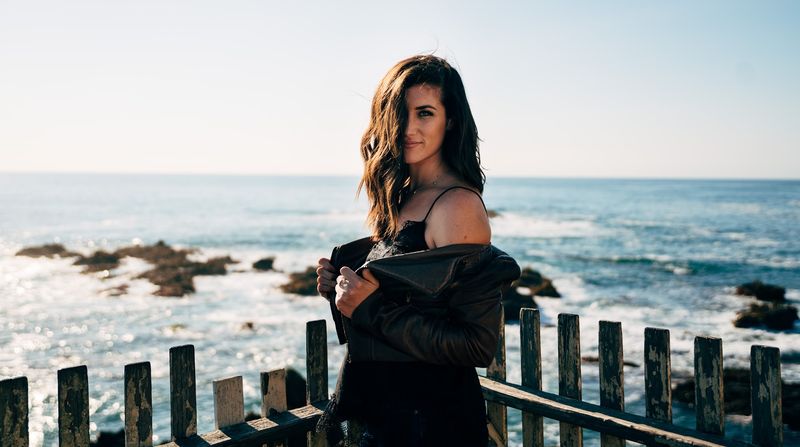 Jacket held open, hair across her face, sidelong look