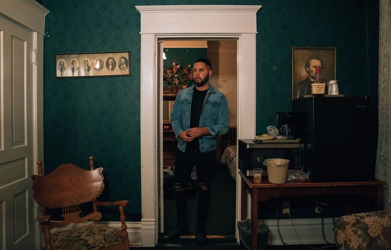 Man stands in a far doorway of a green-papered room, a portrait on the wall