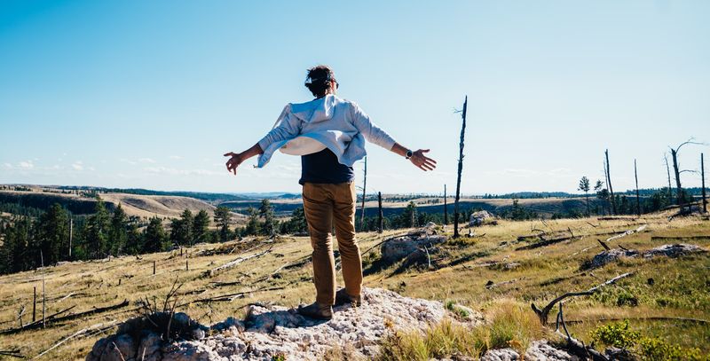 Man from behind, arms wide, open shirt blowing, on a rock outcrop