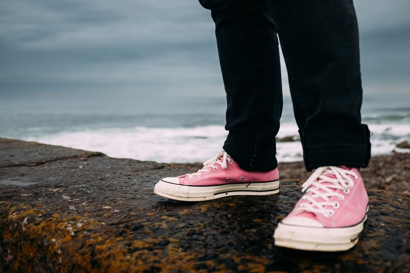 Pink sneakers on wet pier stone, surf behind