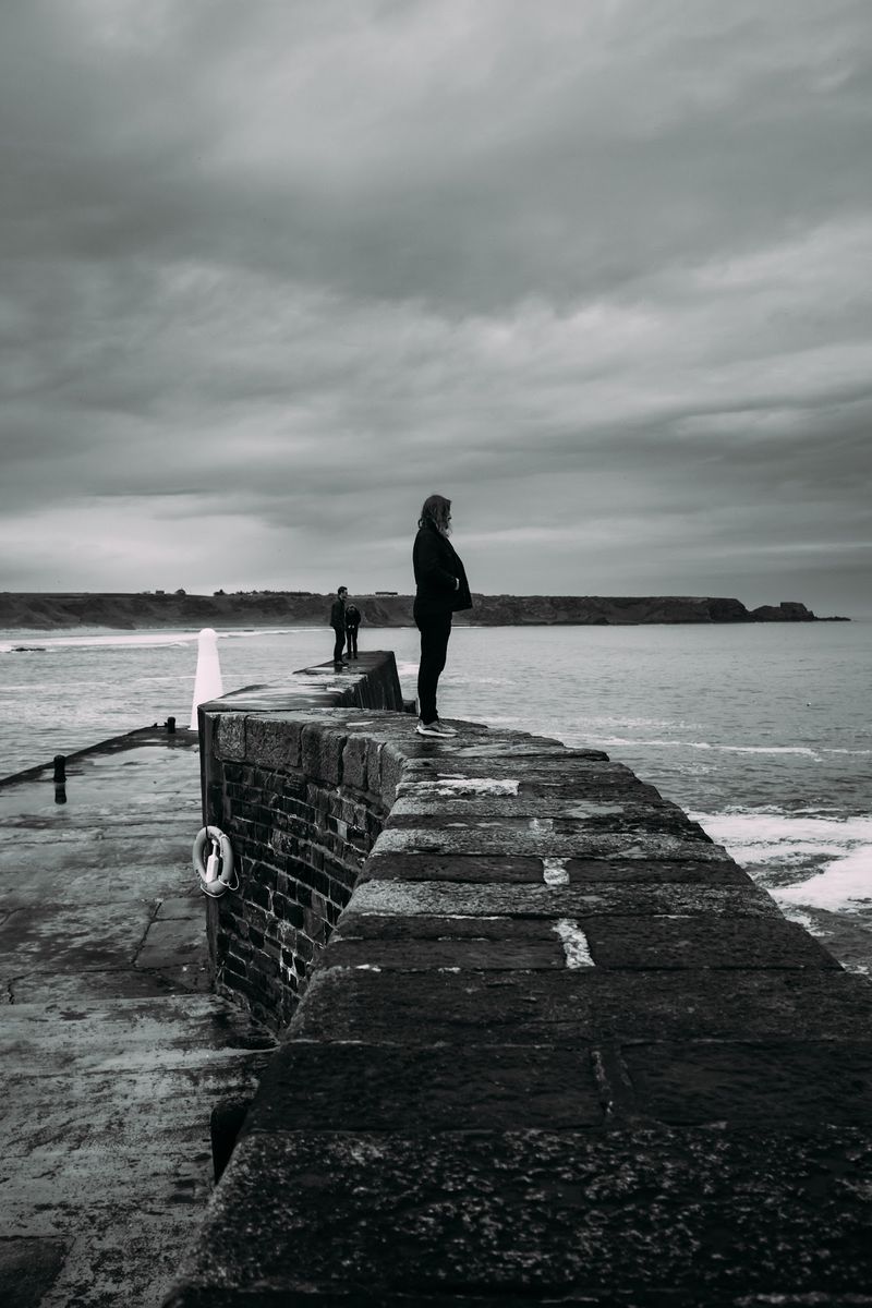 Black and white pier, tiny figure at its end, storm sky