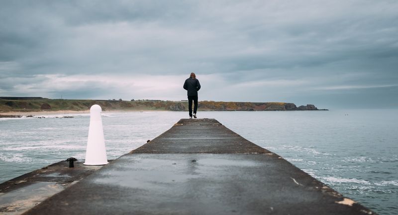 Lone figure at the end of a pier, white bollard leading in