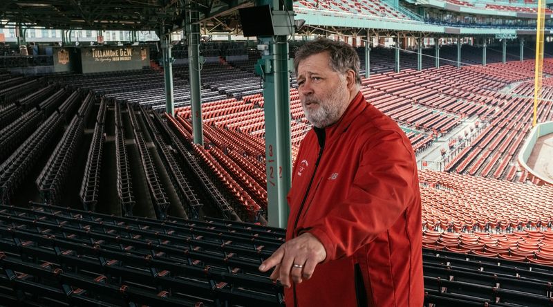 Red-jacketed man mid-story among empty red ballpark seats