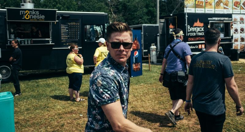 A man in sunglasses and a floral shirt looks back on a festival lawn