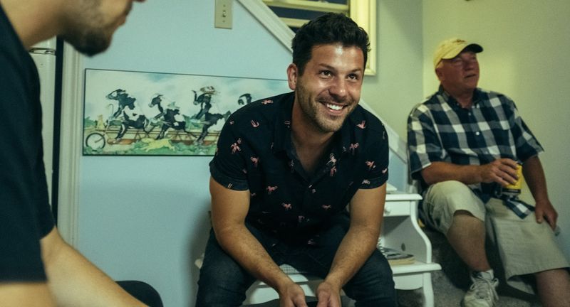 A man in a floral shirt laughs on the stairs beside an older man in plaid