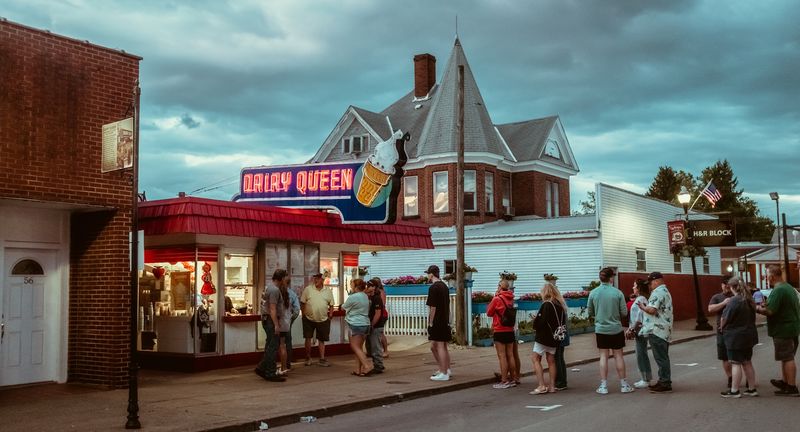 Line outside a neon Dairy Queen under a stormy dusk sky