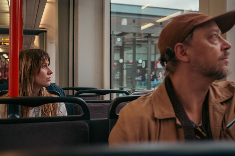 Man in a cap and a woman behind him look the same way on a tram