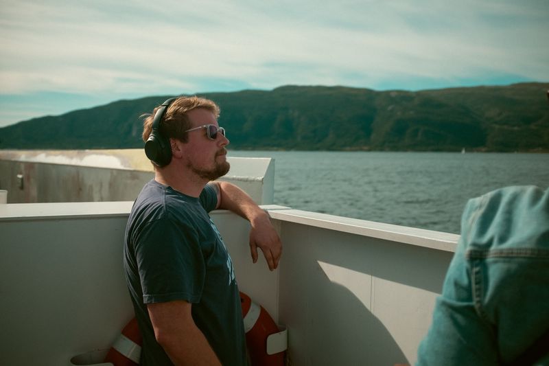 Headphones and sunglasses at ferry rail, fjord hills behind