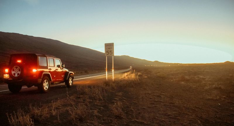 Red Jeep taillights and a 55 sign on a dusk hillside road