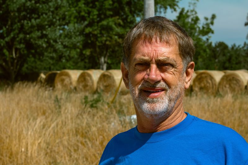 Close portrait of a bearded man, blue tee, hay bales