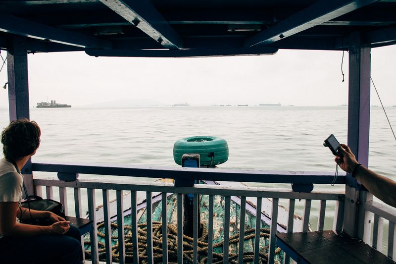 Ferry deck: woman at the rail, a raised phone, teal buoy, rope