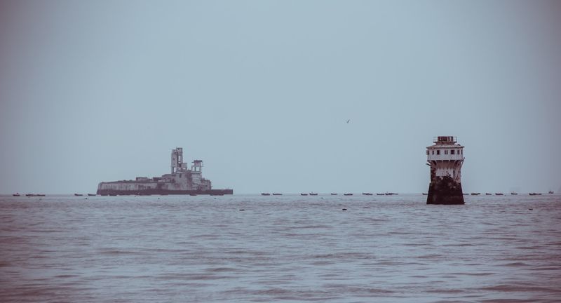 Ruined sea fort and a red lighthouse on flat lilac water